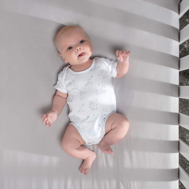 baby lays on grey cot bed fitted sheet