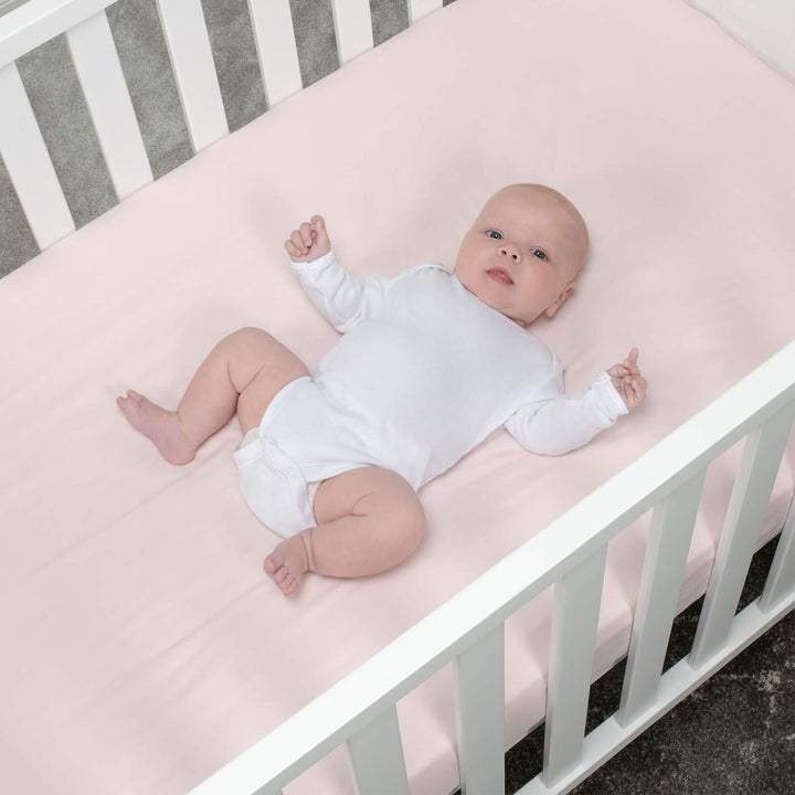 baby lays on pink cot bed fitted sheet