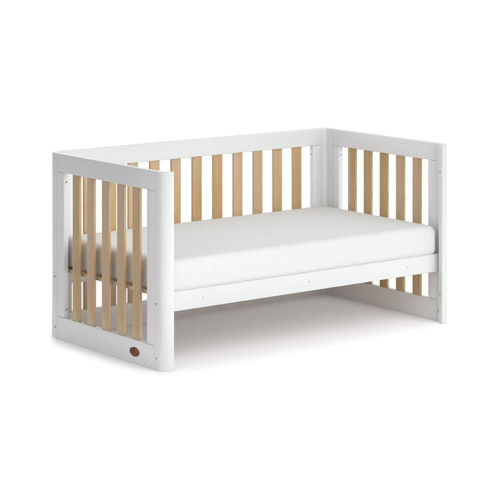 white toddler bed with wooden spindles, rounded corners and feet